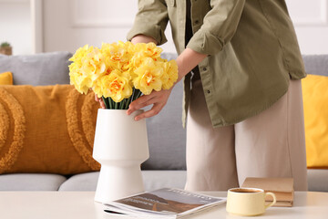Female hands touching daffodil flowers in vase in living room
