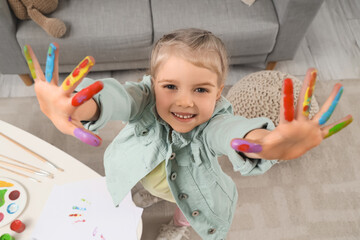 Cute little girl with her fingers in paint at home, closeup
