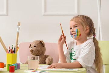 Funny little girl with brush painting at table in bedroom