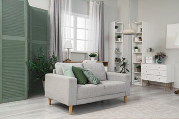 Interior of living room with green folding screen, sofa and shelf units