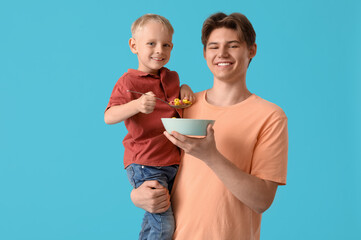 Happy father and his little son with bowl of cornflakes on blue background