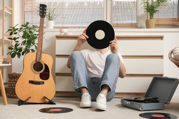 Young man with vinyl disks and record player listening to music at home
