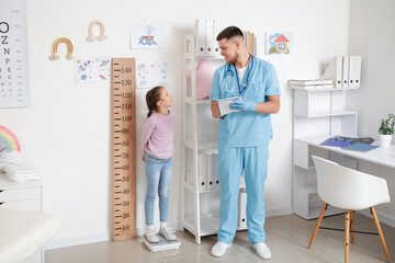 Male pediatrician measuring little girl's weight in clinic
