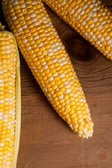 Close up view of three cobs sweet corn with green leaves on wooden background..