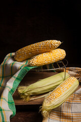 Several cobs sweet corn with green leaves on wooden background..
