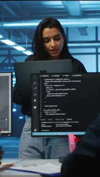 Vertical video Portrait of smiling Indian manager in server room managing team of engineers looking for equipment misconfigurations. Happy team leader coordinating employees checking data center