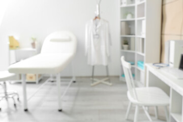 Blurred view of medical office with couch, shelf units and doctor's workplace