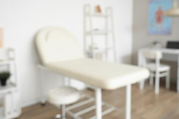 Blurred view of medical office with couch, shelf unit and doctor's workplace