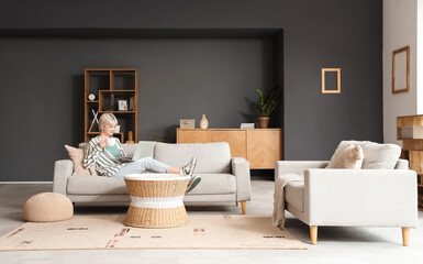 Young woman with cup of coffee using laptop on sofa at home