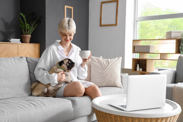 Young woman with cup of coffee and pug dog sitting on sofa at home