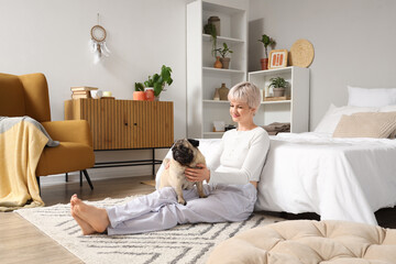 Young woman with pug dog sitting on carpet in bedroom