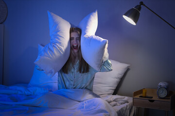 Stressed young woman with pillows suffering from insomnia in bedroom at night