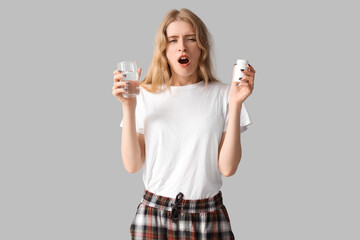 Tired young woman with sleeping pills and glass of water on light background