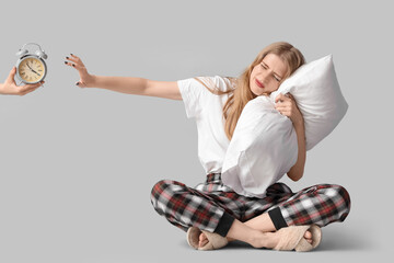 Young woman with pillow suffering from insomnia and alarm clock on light background