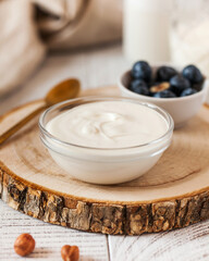 Rich creamy yogurt in a glass bowl on a wooden round, accompanied by fresh blueberries 