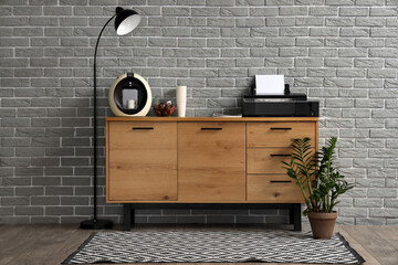 Modern printer and coffee machine on commode near grey brick wall in office
