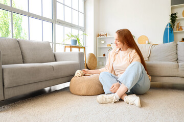Beautiful redhead woman with cute white rat on pouf at home