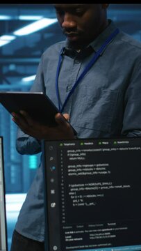 Vertical video Technician in server hub using tablet to find hardware misconfigurations affecting rackmounts performance. Man checking data center infrastructure devices bottlenecks leading to errors