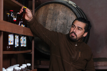 A man takes a bottle of wine in a wine cellar to check the product