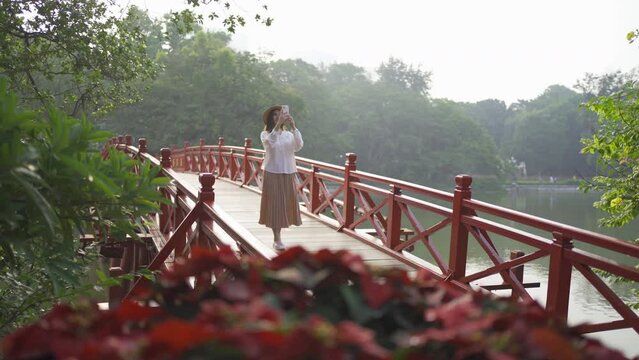 Portrait of Asian Vietnamese woman travel in The Red Bridge in public park garden with trees in Hoan Kiem Lake in Downtown Hanoi. Urban city, Vietnam..