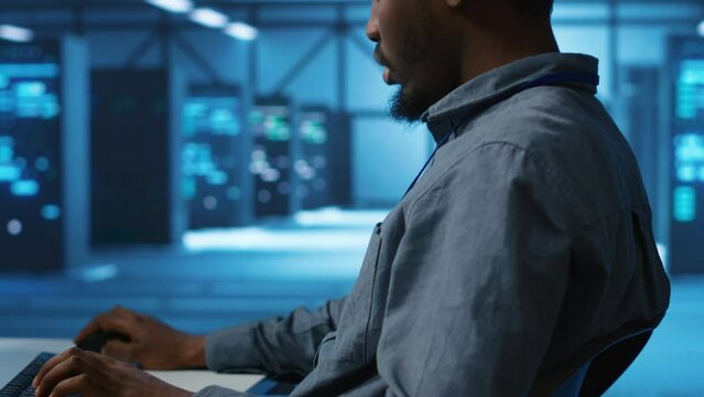 African american man working in server hub capable of processing vast amounts of data. IT programmer at PC desk typing on keyboard, updating servers controlling network resources, close up shot