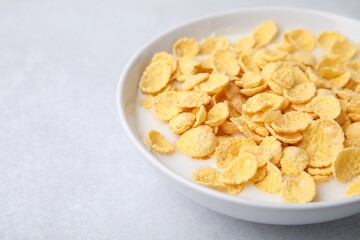 Breakfast cereal. Corn flakes and milk in bowl on light grey table, closeup. Space for text