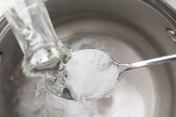 Pouring vinegar into spoon with baking soda over saucepan, above view