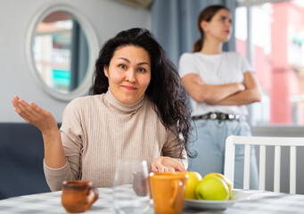 Upset disappointed woman sitting at home while girl calming her, asking to forgive after argument