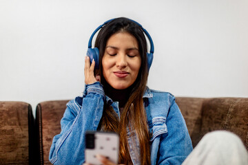 Woman with Blue Headphones Enjoying Music on a Brown Sofa