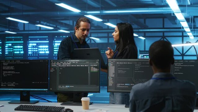 Multiethnic team of admins working in high tech server room capable of storing vast amounts of data. Diverse colleagues doing brainstorming, discussing ways to fix servers