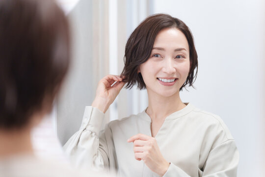 鏡を見て髪の毛を触るミドル女性（美容・ヘアセット・ヘアケア・髪の毛）