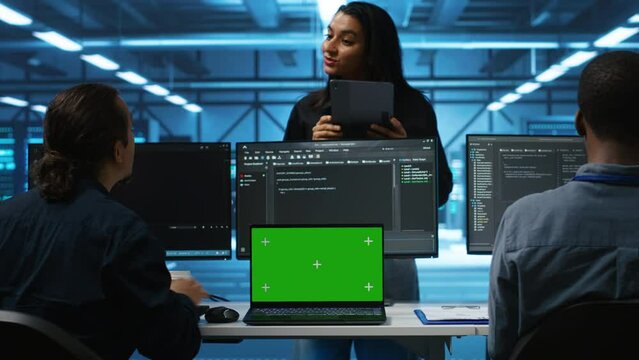 Supervisor in server hub managing diverse team of developers using green screen laptop looking for misconfigurations. Manager coordinating experts mending data center bugs with chroma key notebook