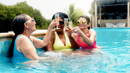 Fototapeta premium Senior people enjoy pool party during summer vacations at luxury hotel. Happy women friends cheering with champagne