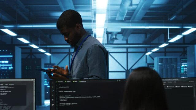 Technician doing system analysis using tablet, doing needed adjustments in supercomputers server farm. Engineer overseeing data center housing storage infrastructure supporting critical IT workloads
