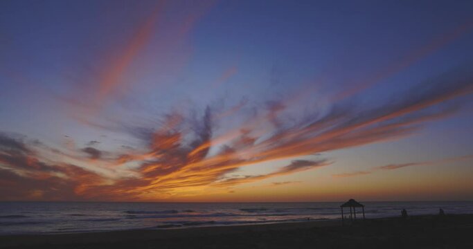 People on the beach silhouette at sunset with calm ocean waves and purple orange clouds