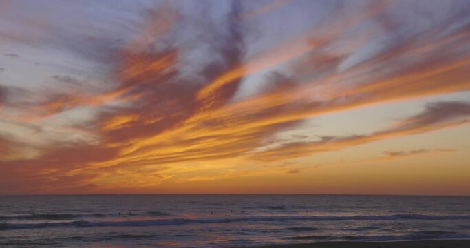 Tropical beach at sunset with dramatic orange sky and people swimming in ocean with calm waves