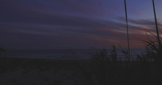 Playa de El Palmar beach at sunset on Spanish coastline with people walking and calm waves with orage dramatic purple sky