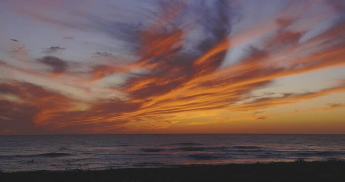 Beach at sunset and people in the calm water with dramatic orange purple sky