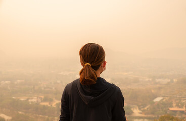 Rear view of Asian woman looking to her town covered with PM2.5 pollution.