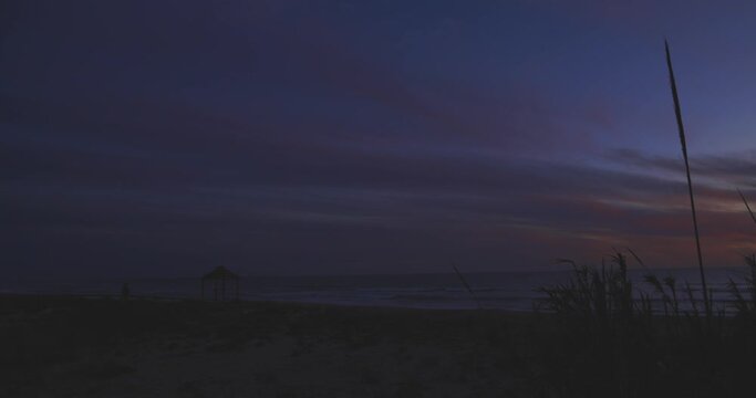 Tropial beach in summer at sunset on Spanish coastline with people walking and calm waves with orage purple sky