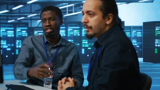 Upbeat african american computer scientist and coworker upgrading equipment in data center. Joyous admin at PC desk in high tech facility overseeing server clusters helped by colleague