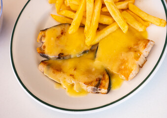 Roast swordfish slices in hollandaise sauce with French fries dished up in a plate