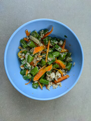 A blue bowl brimming with sautéed green beans, carrots, and eggs invites you to indulge in a colorful, nutritious feast. The vibrant vegetables blend harmoniously with the fluffy, golden eggs.