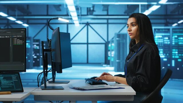 Computer scientist working in high tech server hub capable of processing vast amounts of data. Woman at PC desk typing on keyboard, updating servers controlling network resources