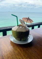 Fresh coconut drink on the wooden table with seascape background. 