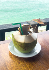 Fresh coconut drink on the wooden table with seascape background. 