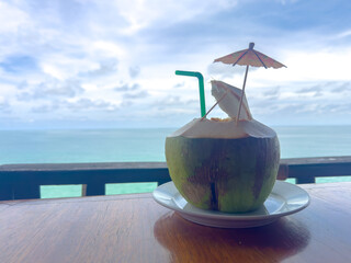 Fresh coconut drink on the wooden table with seascape background. 