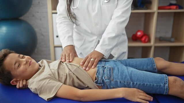 A female doctor treats a young boy's abdomen in a physiotherapy clinic, suggesting digestive rehabilitation.