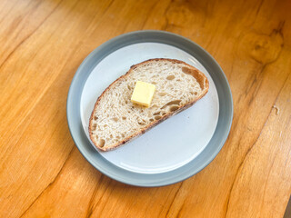 A piece of sliced sourdough bread on top with butter served on the plate.