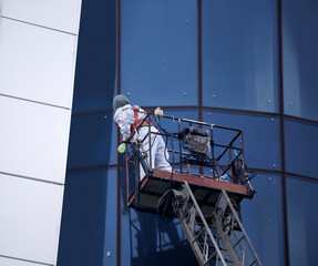 An installer dressed in a uniform and a safety harness cleans the glass facades while standing on a construction winch